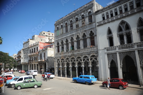 Brightly colored classic American cars serving as taxis pass on the main street in front of the Capitolio building in Central Havana, Cuba © porpendero