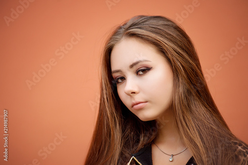 Female portrait of brown-haired woman with long hair in fashion style on the street close-up on a red wall background.