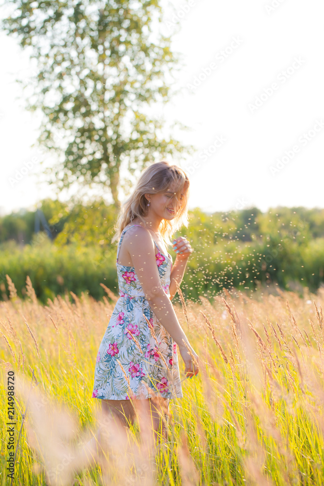 Beautiful young woman standing in a field, green grass and flowers. Outdoors Enjoy nature. Healthy smiling girl standing in tall grass