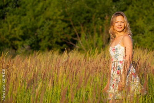 Beautiful young woman standing in a field, green grass and flowers. Outdoors Enjoy nature. Healthy smiling girl standing in tall grass