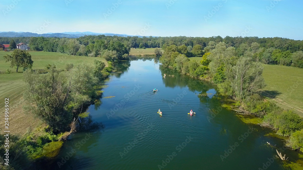 AERIAL: Flying behind a group of active tourists canoeing down a calm river.