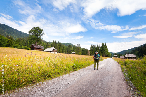 Hiker with backpack walking along dirt road to a forest