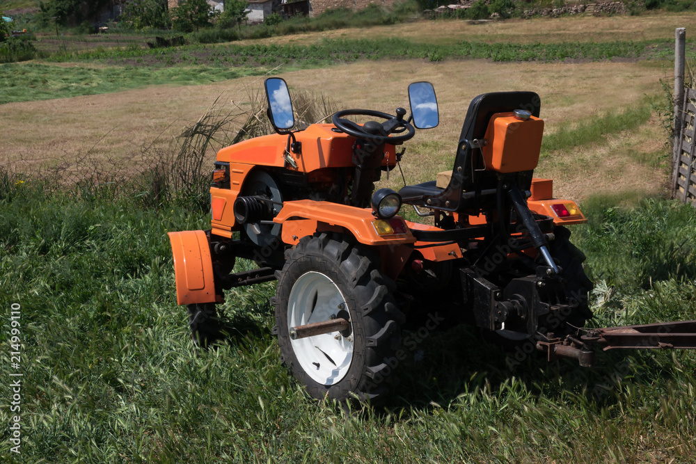 Tractor on the field/ The orange minitractor works in the field. Agricultural multifunction machine with a trailer collects the harvest. Tractor on the field/ The orange minitractor works in the field. Agricultural multifunction machine with a trailer collects the harvest.