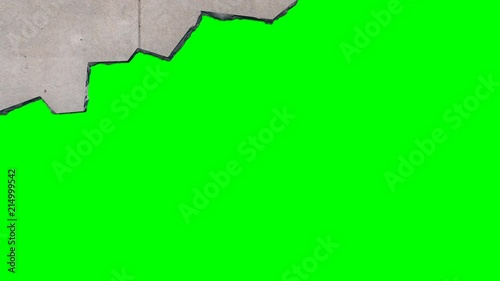 Exploding and crumbling concrete wall with flying debris revealing a green screen background. 