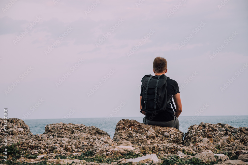 Man by the sea. Young traveler at the sea. Man is looking into the distance. Tourist with a backpack. Background for travel. Holidays in hot countries. Coast Side, Turkey.