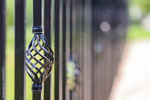 Black decorative metal fence, angular iron rods and curved upper part. Close-up of the decoration on the side.