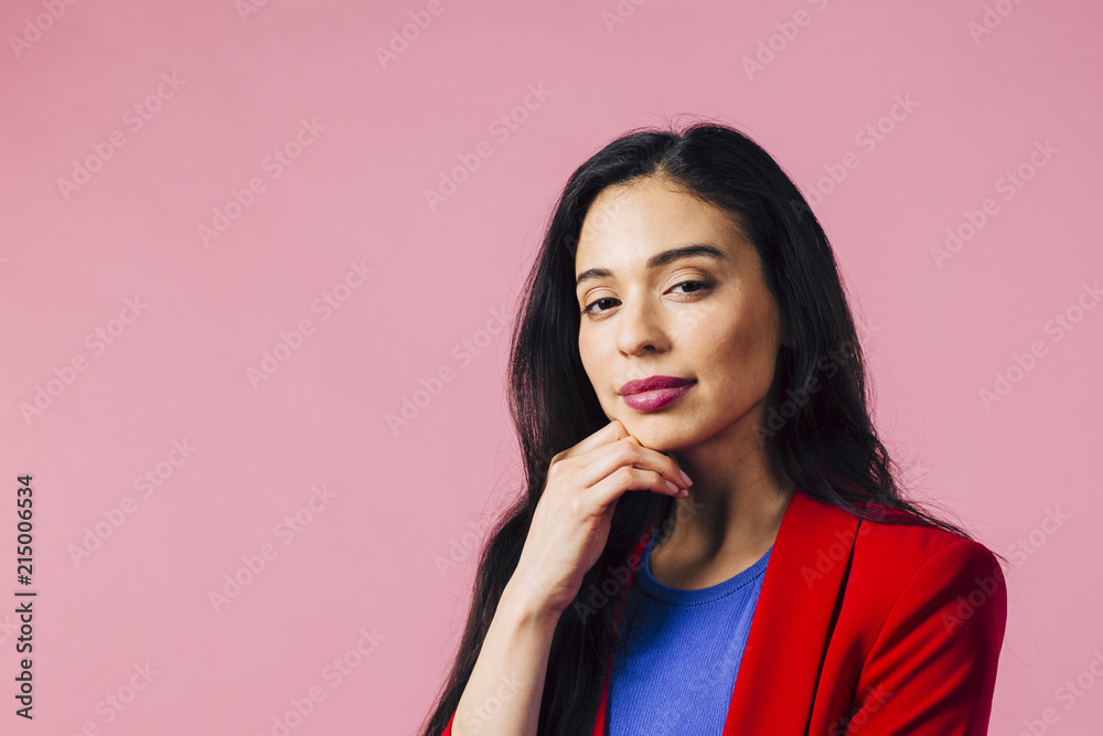 Attractive young brunette with hand on chin looking at camera, isolated on pink studio background Attractive young brunette with hand on chin looking at camera, isolated on pink studio background