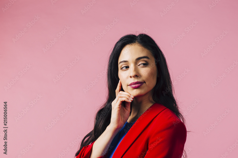 Portrait of a smiling young brunette in red jacket and finger on cheek, isolated on pink studio background Portrait of a smiling young brunette in red jacket and finger on cheek, isolated on pink studio background