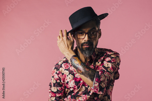  Portrait of a very cool mature artist with tattoo and glasses, touching his hat, isolated on pink studio background photo