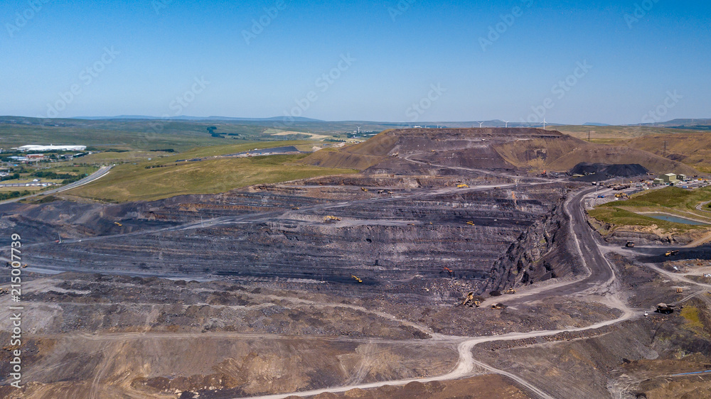 Aerial drone view of a huge opencast coal mine cut into a rural hilly area