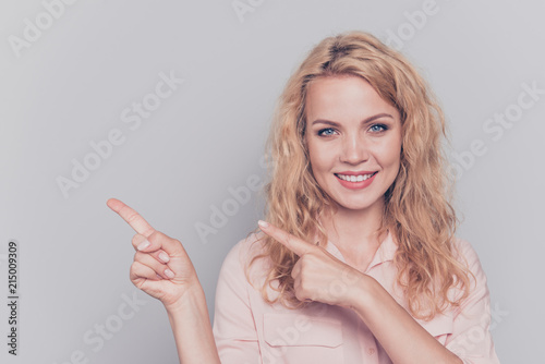 Attractive cute curly-haired blonde gorgeous caucasian charming young smiling girl wearing formal wear shirt pointing fingers. Copy space. Isolated over grey background