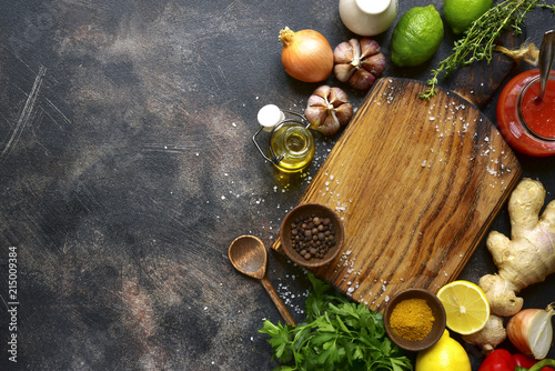 Food background with empty wooden cutting board and ingredient for cooking : vegetable,spices, ,salt, herb, sauce, citrus fruits.Top view with copy space.