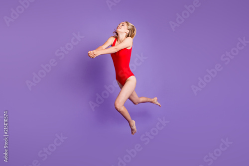 Concept of a beach holiday. Full-size portrait of young blonde girl jumped up to fight off a pitch of a volleyball isolated on violet background