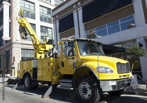Yellow construction excavator with auger parked on urban street.