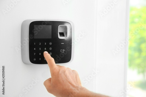 Mature man entering code on alarm system keypad indoors