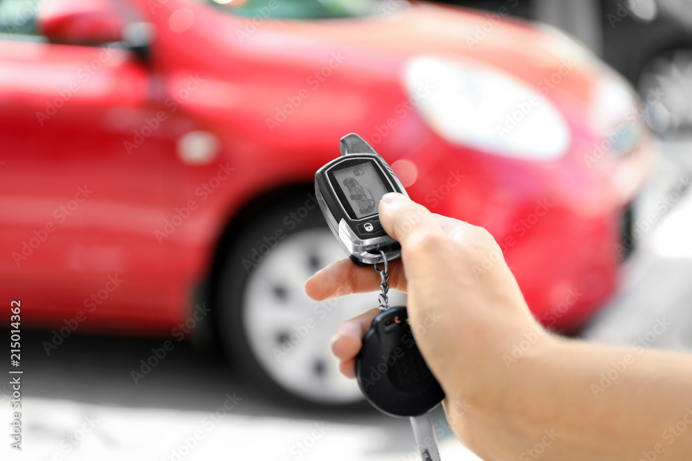 Fototapeta premium Young woman pushing button on remote control of car alarm system, outdoors