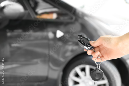 Young woman pushing button on remote control of car alarm system, outdoors