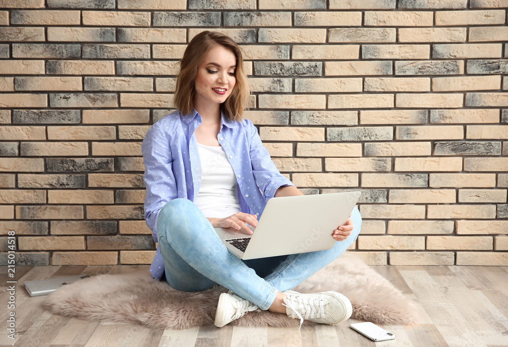 Beautiful young woman using laptop while sitting on floor near brick wall Beautiful young woman using laptop while sitting on floor near brick wall