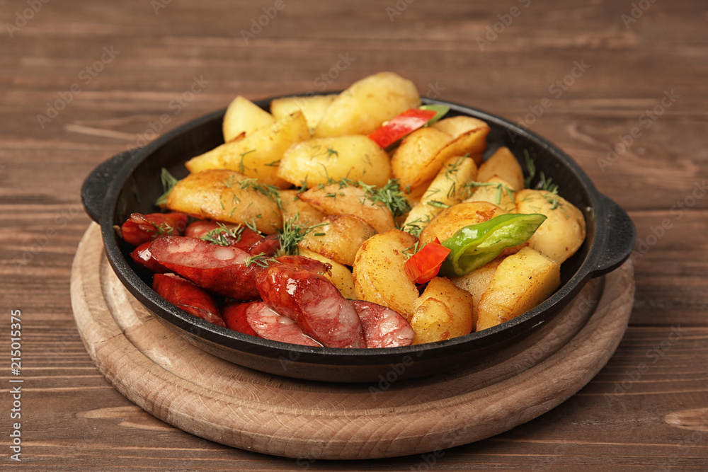 Pan with fried potatoes and sausages on wooden table