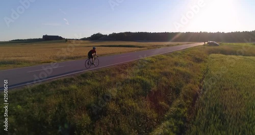 Man biking on the countryside, C4K aerial view closing in on a biker driving on a road, between wheat fields, on a sunny summer evening sunset, in Uusimaa, Finland