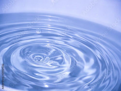 Close up blue water drop falling into water making a reflection concentric circles. Blue wave.