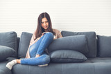 Beautiful Asian girl in jeans is smiling and sitting on  couch on the sofa using her smartphone in a luxury room.