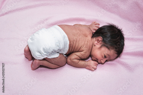 Multiracial newborn laying alone on a pink blanket