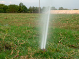 Close view of in-ground sprinkler spraying a unkempt field littered with dead grass