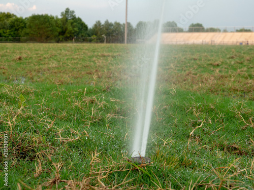 Close view of in-ground sprinkler spraying a unkempt field littered with dead grass