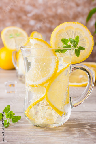 Refreshing mineral water with lemon, mint and ice cubes in glasses on a wooden table