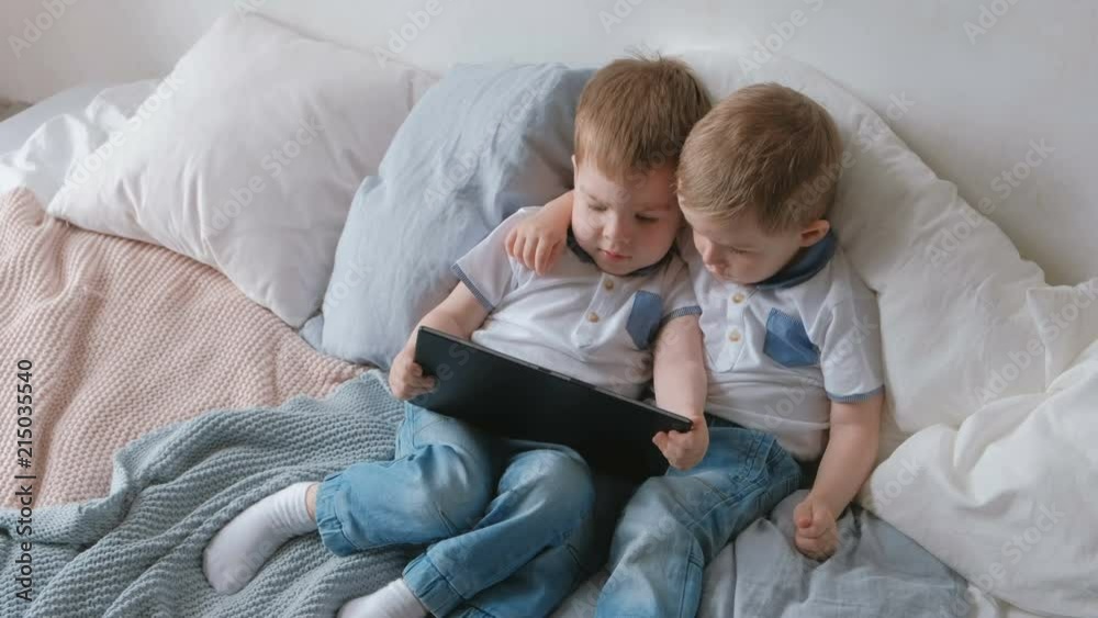 Kids with tablet. Two boys twins toddlers looking cartoon at tablet lying on the bed. Kids with tablet. Two boys twins toddlers looking cartoon at tablet lying on the bed.