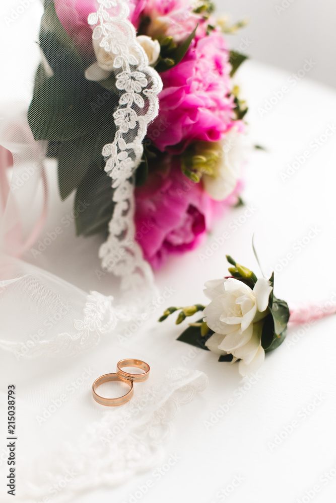 Beautiful pink peonies bouquet and wedding rings lie on a white table. Top view. Beautiful pink peonies bouquet and wedding rings lie on a white table. Top view.