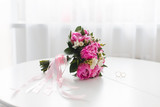 Beautiful pink peonies bouquet  and wedding rings lie on a white table. 