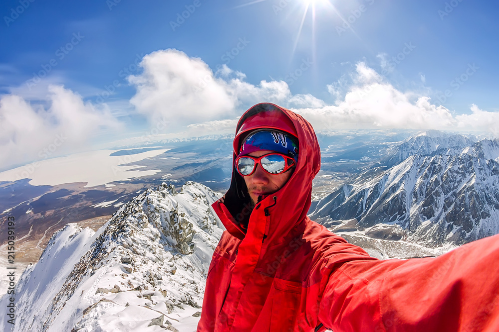 Selfi male mountaineer in snowy mountains, wearing a helmet with a backpack