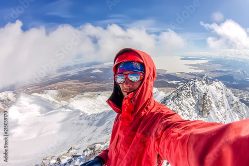 Selfi male mountaineer in snowy mountains, wearing a helmet with a backpack