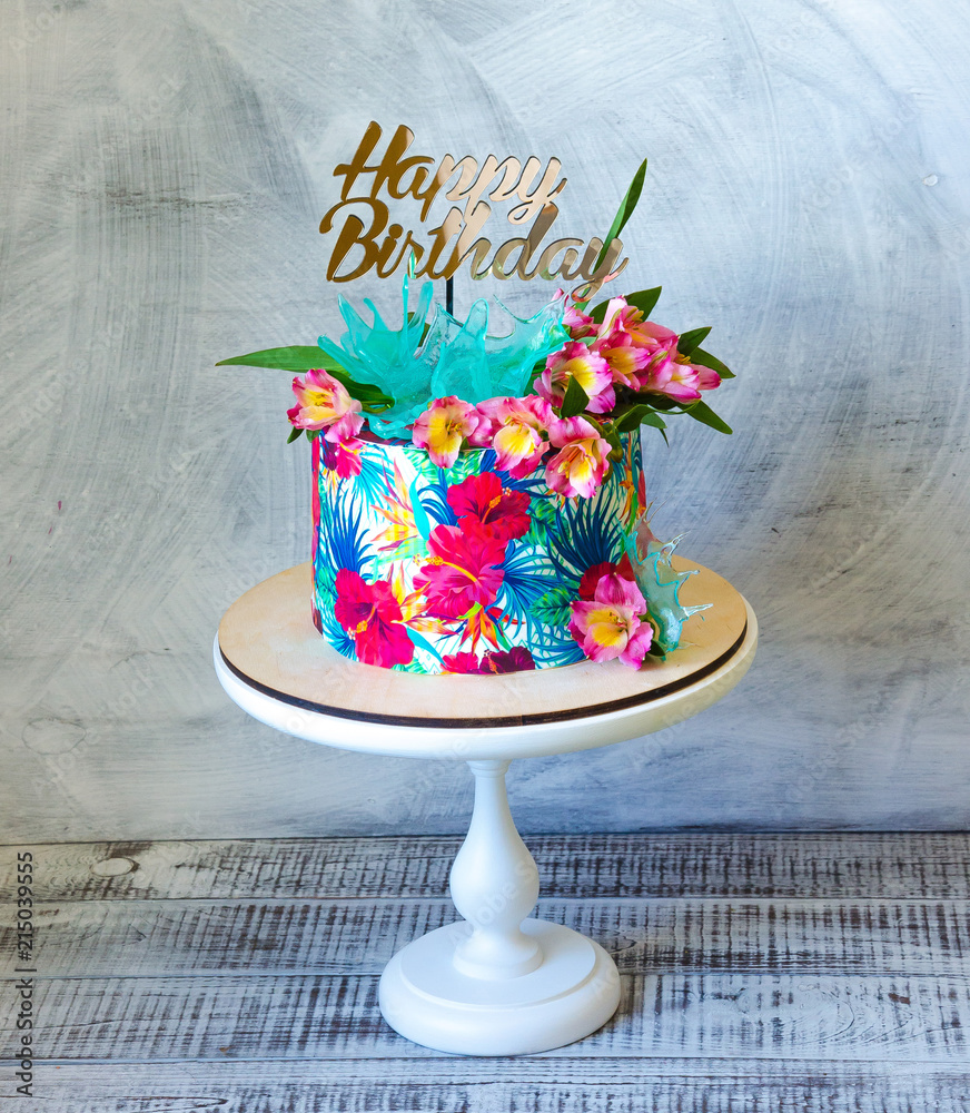 Tropical birthday cake on a cakestand with a topper Photos | Adobe Stock