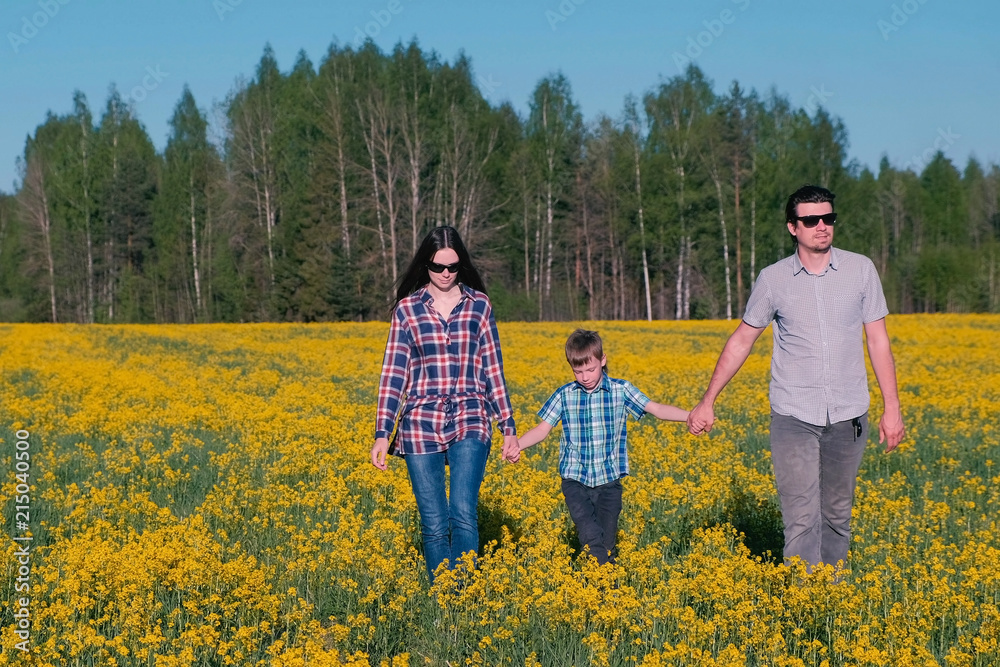 Family walk on the field with yellow flowers near the forest. Mom, son, dad.
