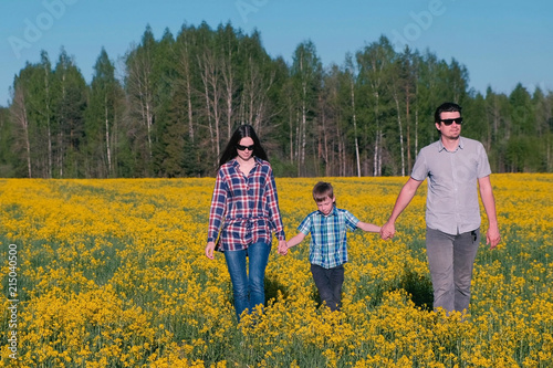 Family walk on the field with yellow flowers near the forest. Mom  son  dad.