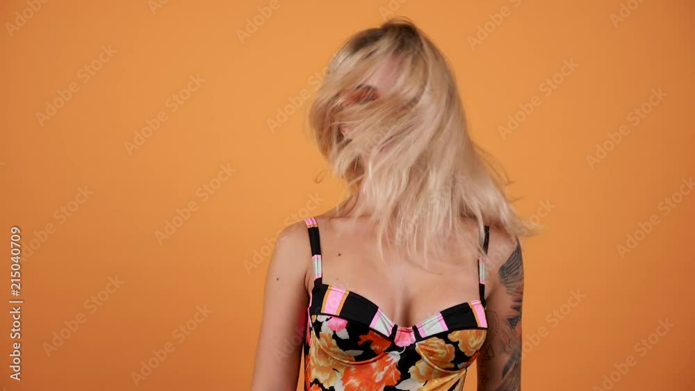 Beautiful woman shaking her head and blowing the hair in slow motion footage on orange yellow background