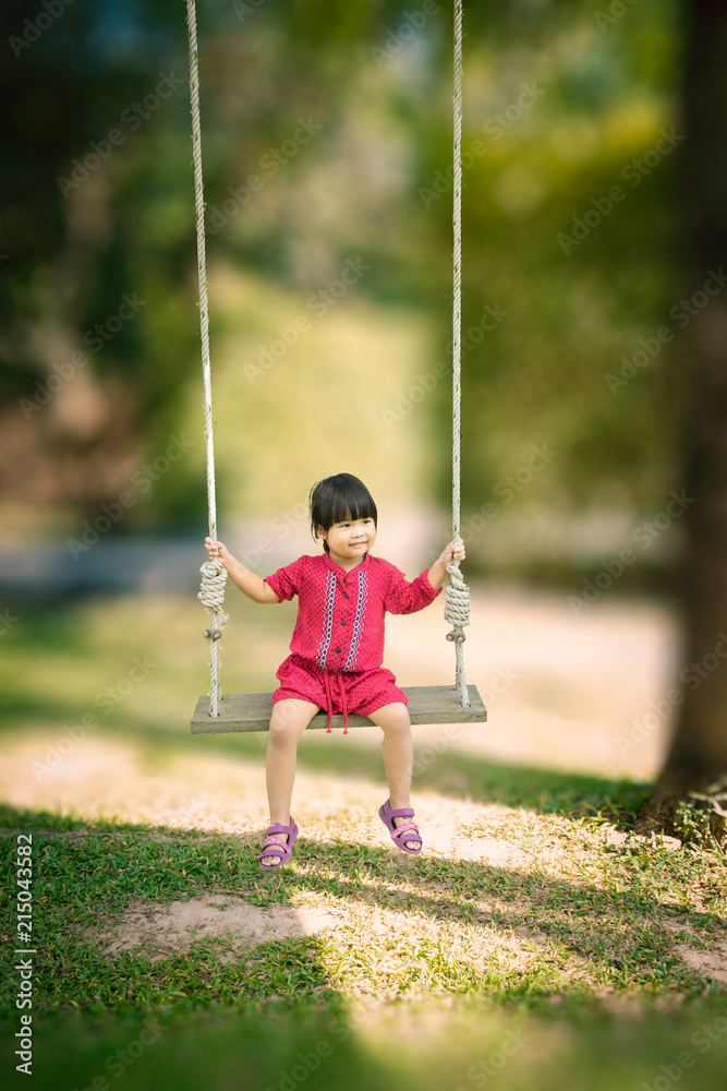Little girl in red dress sitting on a swing in the park