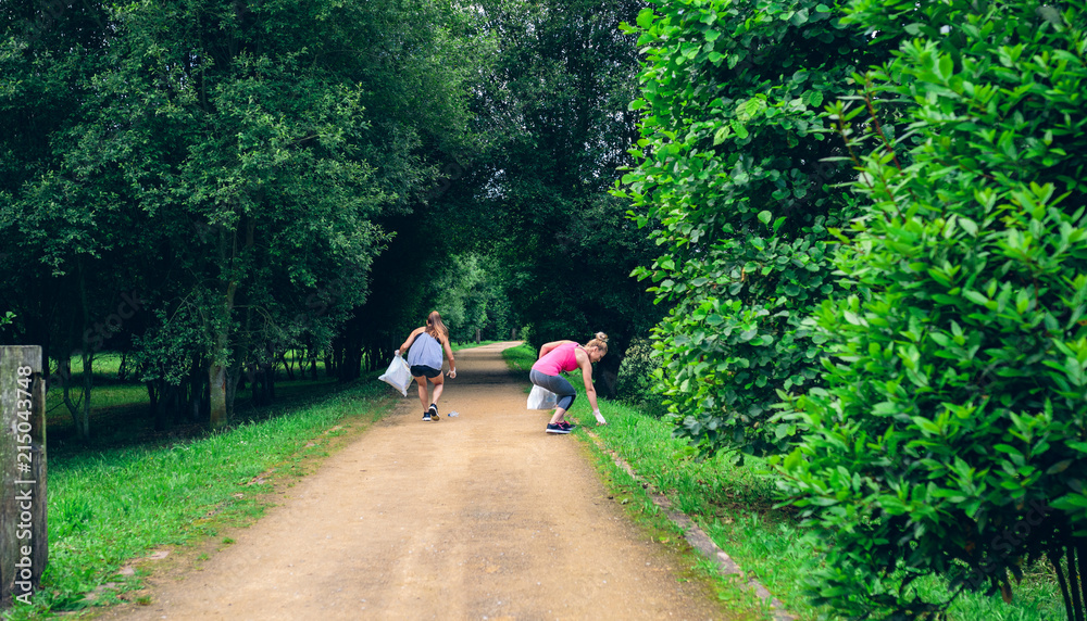 Two girls on back with garbage bags doing plogging Two girls on back with garbage bags doing plogging