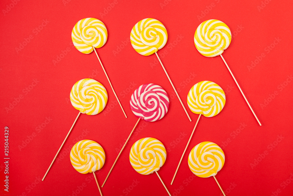 Sweet caramel candy on a red background. Bright lollipops. Yellow and pink sweets from the confectioner.