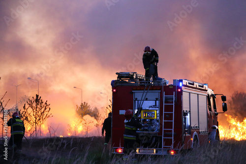 Team of fire fighters fighting fire in the evening. Fire truck on the flames and smoke background.