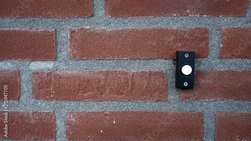 background of a red stone wall with a black with white doorbell button. photo