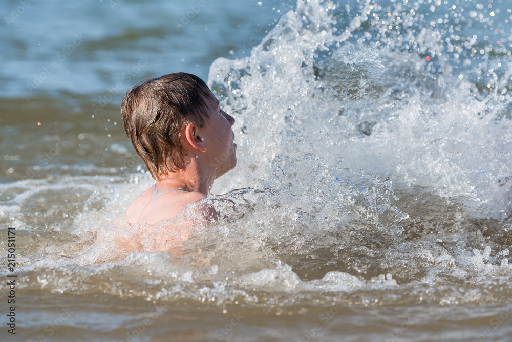 A boy teen swims in a spray of water - a concept of a beach holiday