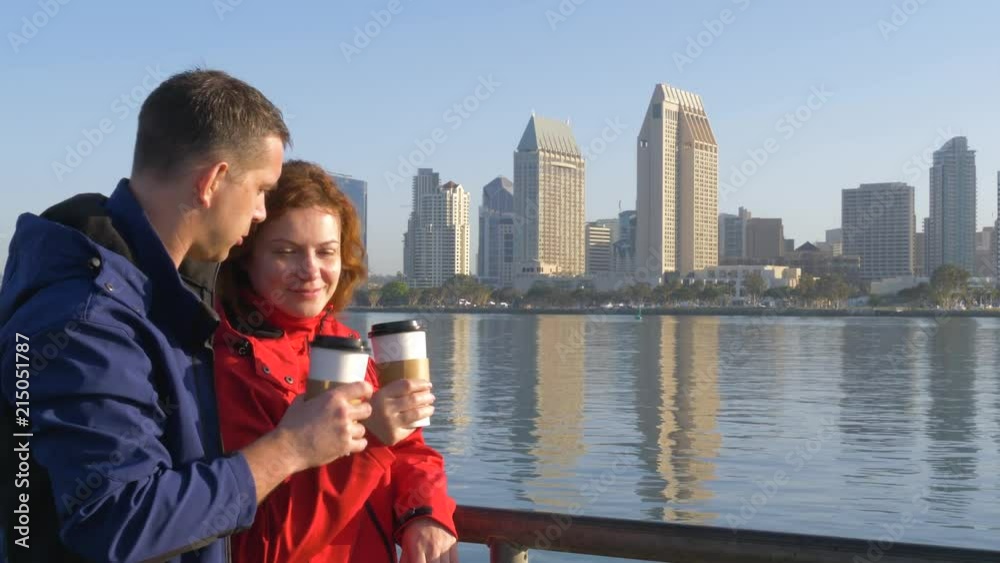 Loving couple on a journey drinking coffee in San Diego. Young couple looks at an urban landscape in San Diego in early morning and shares impressions of a romantic journey. View of downtown San Diego