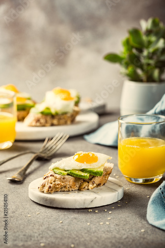 Healthy sandwich with fresh avocado and fried quail egg on small marble board on gray background. Breakfast or lunch food concept with copy space. Retro style toned.