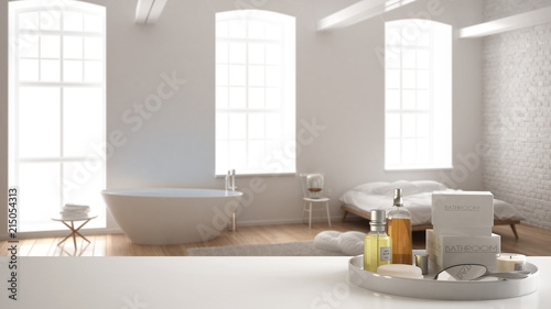 Spa  hotel bathroom concept. White table top or shelf with bathing accessories  toiletries  over blurred minimalist bathroom with bedroom  modern architecture interior design