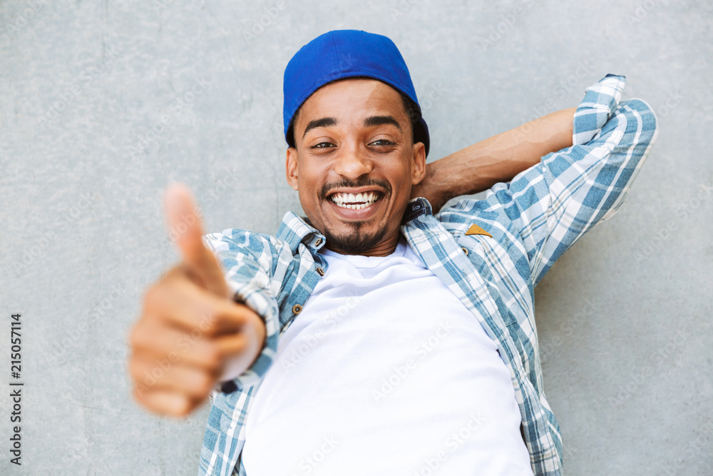 Naklejka premium Smiling young african guy laying on a concrete outdoors