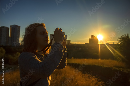 A young man is photographing something on the background of the setting sun